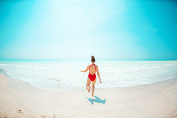 Seen from behind young woman in red beachwear on beach running