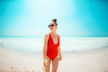 smiling young woman in red swimwear on seashore walking