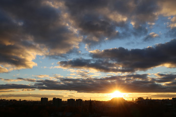 Sunset over the big city. Dark clouds in the sky, setting shining sun and silhouettes of buildings