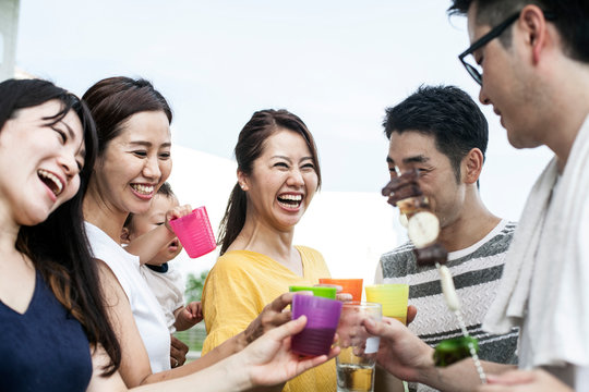 Group of cheerful young Japanese men and women standing outdoors, toasting with plastic beakers.