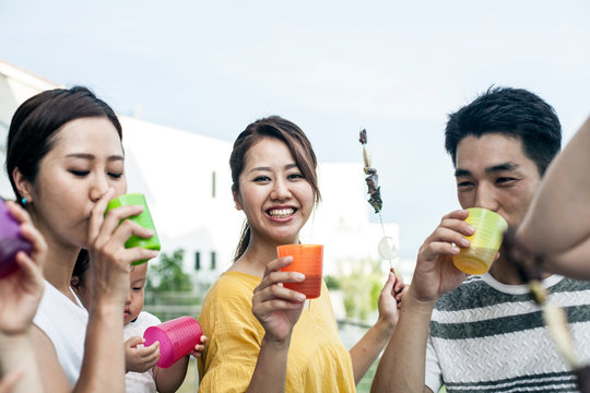 Group of Japanese men and women standing outdoors, drinking from plastic beakers.