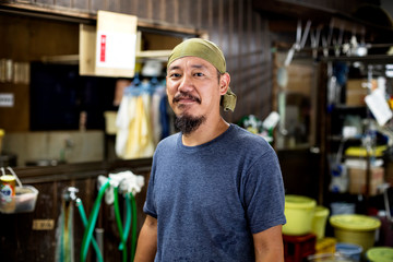 Japanese man wearing bandana in a textile dyeing workshop, smiling at camera.