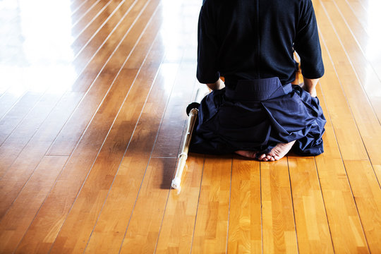 Rear view of Japanese Kendo fighters kneeling on wooden floor.