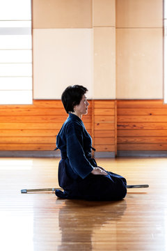 Side view of female Japanese Kendo fighter kneeling on wooden floor.
