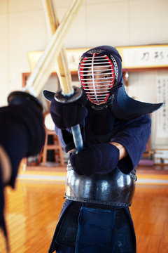 Two Japanese Kendo fighters wearing Kendo masks practicing with wood sword in gym.