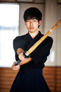 Male Japanese Kendo fighter holding wood sword in combat pose, looking at camera.