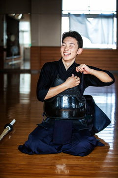 Male Japanese Kendo fighter kneeling on floor, fastening his breastplate.