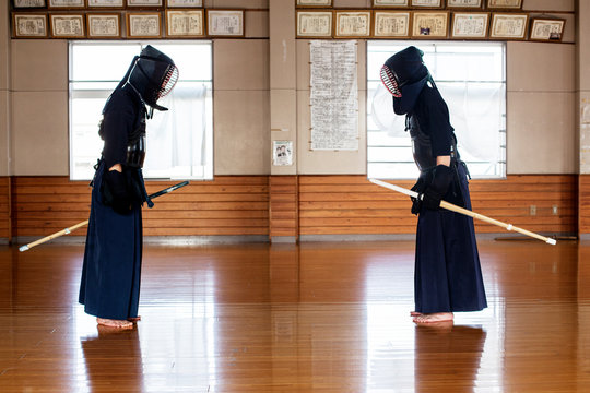 Japanese Kendo fighters standing opposite each other on wooden floor, bowing and greeting.