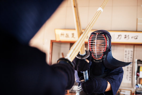 Two Japanese Kendo fighters wearing Kendo masks practicing with wood sword in gym.