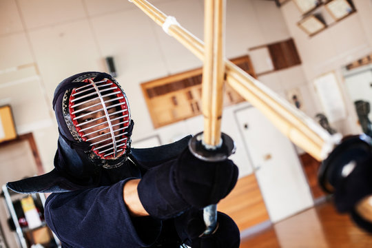 Two Japanese Kendo fighters wearing Kendo masks practicing with wood sword in gym.