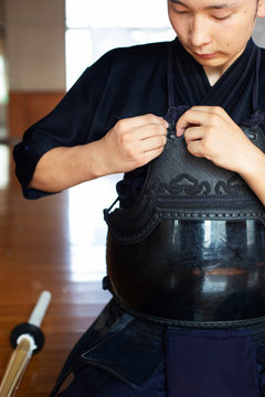 Male Japanese Kendo fighter kneeling on floor, fastening his breastplate.