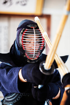 Close up of Japanese Kendo fighter wearing Kendo mask in combat pose.