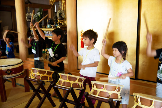 Group of pre-school children playing the drums in a Japanese temple, a traditional religious practise. 