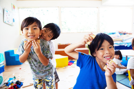 Three young children in a Japanese preschool, looking at camera and pulling faces,smiling.