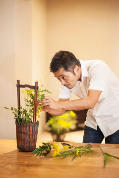 Japanese man standing in flower gallery, working on Ikebana arrangement.