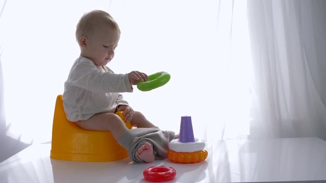 games on potty, developing Baby sitting on chamberpot and playing with educational colored toys pyramid in bright room close-up