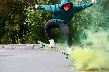 Full length portrait of modern teenager doing skateboard stunts in green smoke, copy space