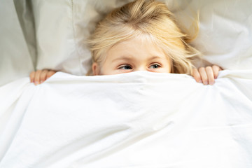 A little girl in bed below the covers