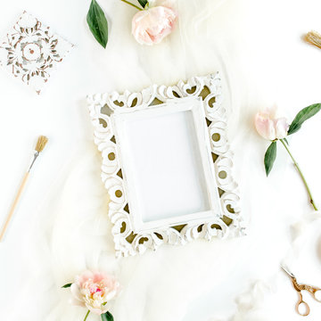 Carved, white frame decorated of white peony flowers, accessories on white background. Flat lay, top view.
