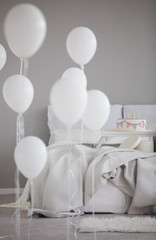 Balloons in front of bed with blanket and pillows in grey simple bedroom interior with fur. Real photo