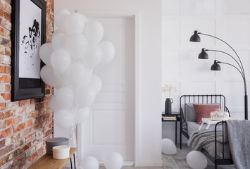 Poster on red brick wall and balloons in bedroom interior with black lamp above bed. Real photo