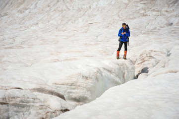 Traveler in a cap and sunglasses with a backpack on his shoulders in the snowy mountains on the glacier against the sky and clouds. Traveler in a natural environment