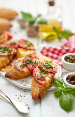 Bruschetta, grilled slices of baguette with mozzarella cheese, tomatoes, garlic and aromatic basil on a white wooden table, close up. A delicious Mediterranean appetizer
