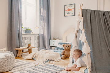 Happy child in tent playing in bedroom interior with plush toy and fox poster above bed. Real photo