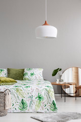 White chandelier above comfortable bed with green and white sheets in stylish bedroom interior, real photo with copy space on the empty grey wall