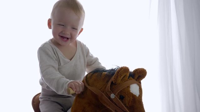 emotion joy of child, cheerful baby boy relish riding on toy equine in room close-up