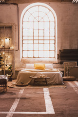 Cushions on bed in spacious industrial bedroom interior with window and wooden bench on carpet. Real photo