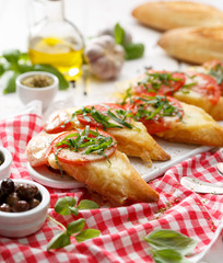 Bruschetta, grilled slices of baguette with mozzarella cheese, tomatoes, garlic and aromatic basil on a white wooden table, close up. A delicious Mediterranean appetizer