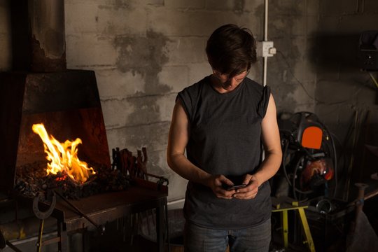 Female metalsmith using mobile phone in factory - Powered by Adobe