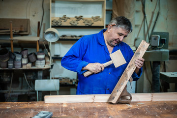 carpenter man repairs the plane with a wooden hammer in the workshop
