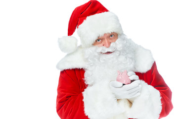 santa claus holding little piggy bank and looking at camera isolated on white