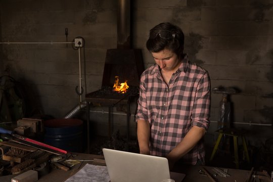 Metalsmith using laptop in factory