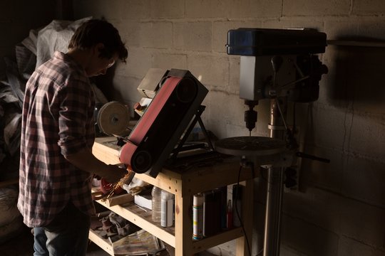 Female metalsmith using sharpening machine - Powered by Adobe