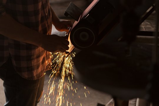 Female metalsmith using sharpening machine - Powered by Adobe