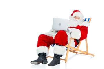 santa claus using laptop while sitting on beach chair isolated on white