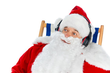 santa claus listening music with headphones while sitting on beach chair isolated on white