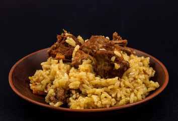 clay plate with rice pilaf, meat, turmeric on black background