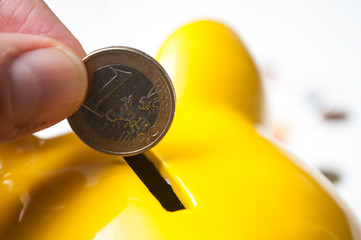 closeup of  hand of man putting euro coin in yellow piggy bank on white background