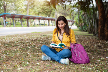 Obraz premium Happy Asian woman sitting and reading books in university park under big tree. People lifestyles and education concept. Summer course and self learning theme. Student and study in college