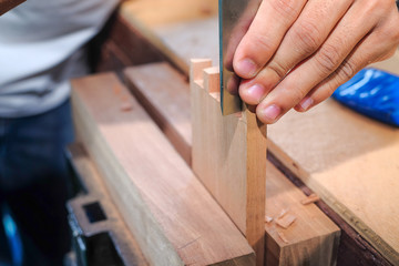 Skilled joiner working in carpentry. Amateur woodworker making dovetail join for wooden drawer in carpenters workshop