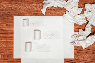 White sheet on a wooden table. Light background image with words on torn paper. Debit, finance, loan.