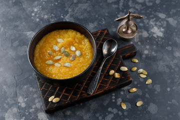 Pumpkin cream soup in a black plate on a dark background.