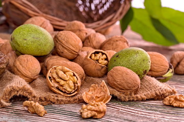 Walnuts with green leaves in garden on the wooden table, on the background wicker basket.