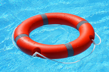 Red lifebuoy pool ring float on blue water. Life ring floating on top of sunny blue water. Life ring in swimming pool