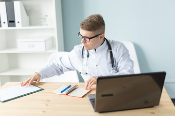 Medicine, working and people concept - handsome doctor sitting at the table and writing a recipe