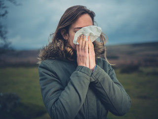 Young woman blowing her nose on the moor